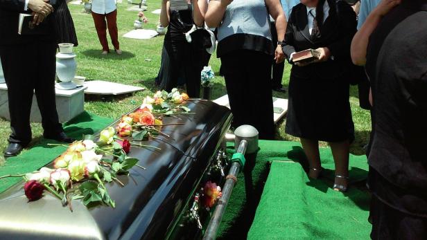 Beerdigung mit schwarzem Sarg Trauernde Menschen stehen um einen schwarzen Sarg mit Blumen auf einem Friedhof