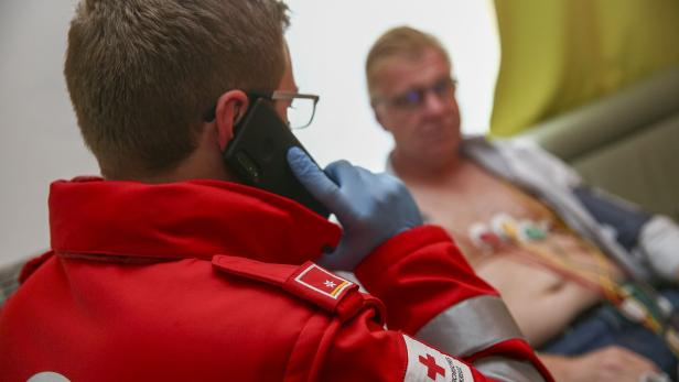 Ein Sanitäter des Österreichischen Roten Kreuzes telefoniert, während ein Patient im Hintergrund liegt.