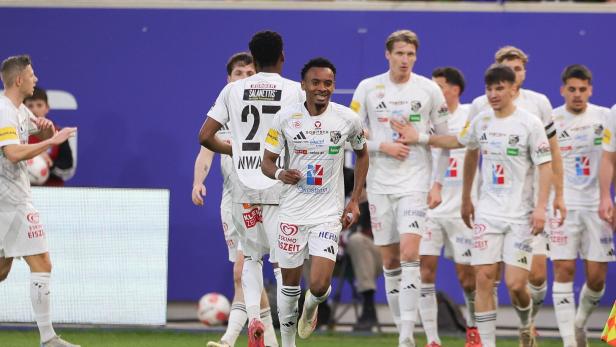 Ein Fußballspieler in weißem Trikot jubelt, umgeben von seinen Teamkollegen.