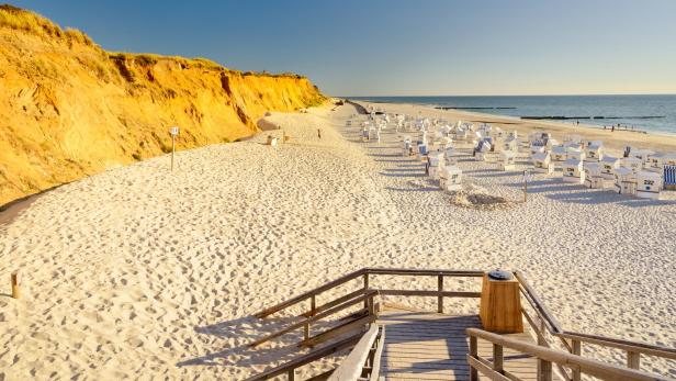 Ein weißer Strand mit Strandkörben und einer Klippe hintendran. 