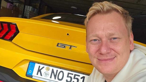 Der Streamer Knossi hat sich mit Fitness-Influencer Sascha Huber eine neue Show überlegt, die unter die Erde geht. Knossi kniet vor einem gelben Auto mit seinem Wunschkennzeichen