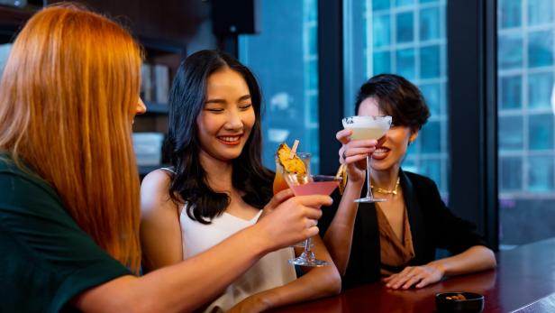 Eine Gruppe von jungen Frauen stößt mit Cocktails an der Hotelbar an.