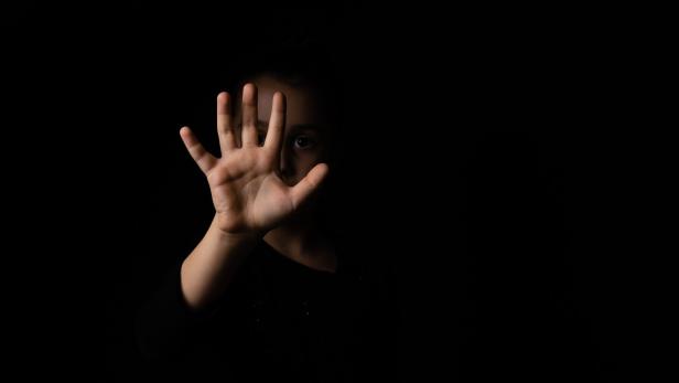 Ein Kind hält die Hand mit gespreizten Fingern nach vorne, das Gesicht ist teilweise im Schatten.
