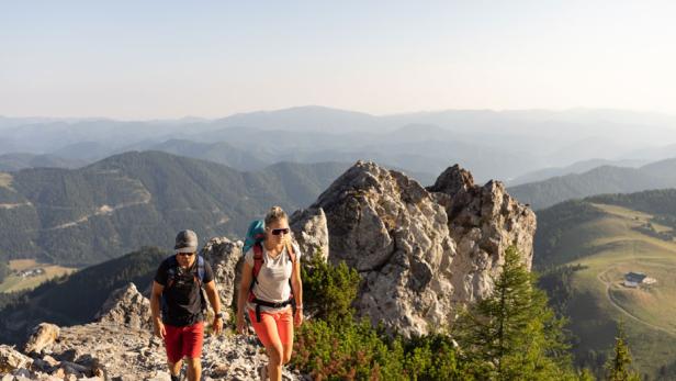 Zwei Wanderer steigen auf einem felsigen Pfad mit Blick auf eine Berglandschaft auf.