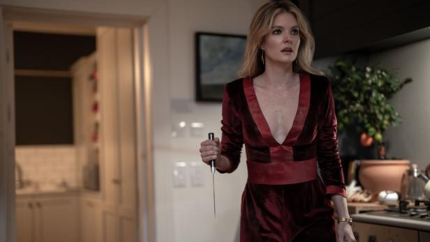 Eine Frau im roten Samtanzug hält ein Messer in einer Küche.