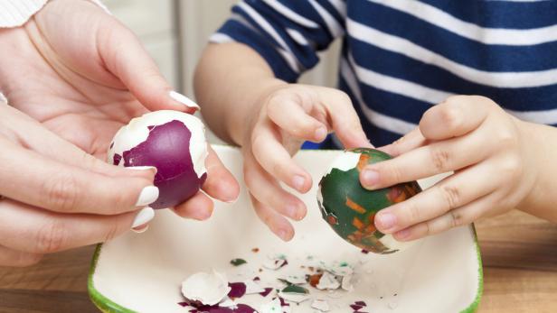 Ein Erwachsener und ein Kind pellen gefärbte Ostereier über einer Schüssel.