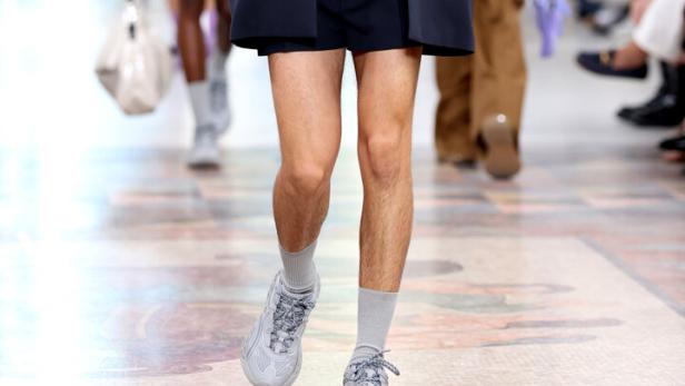 Ein Mann in Shorts, Blazer und Turnschuhen läuft auf einem Laufsteg.