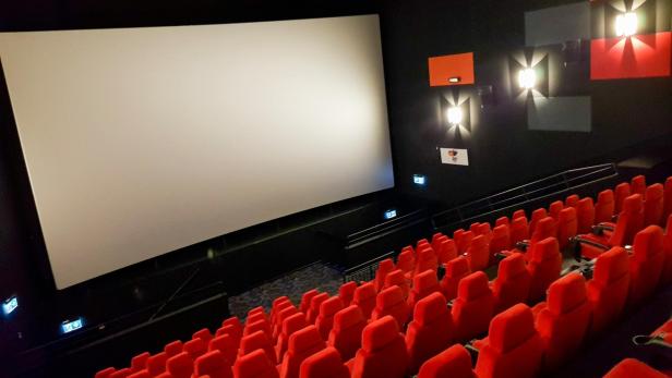 Kinosaal mit roten Sitzen und weißer Leinwand