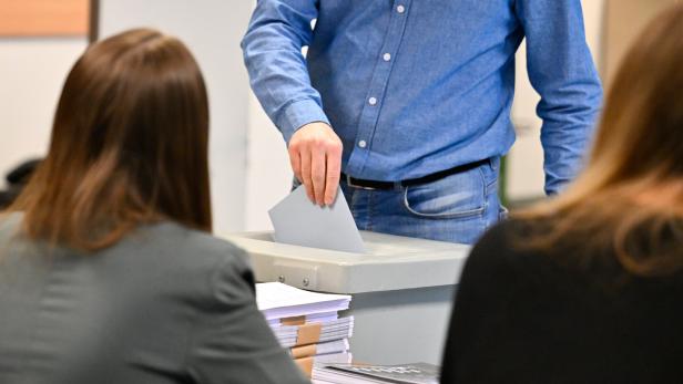 Eine Person wirft einen Stimmzettel in eine Wahlurne.