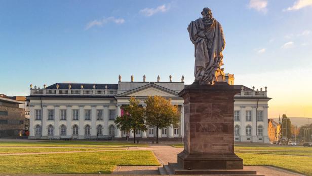 Statue eines Mannes vor einem Gebäude, das die architektonische Schönheit der Umgebung betont.