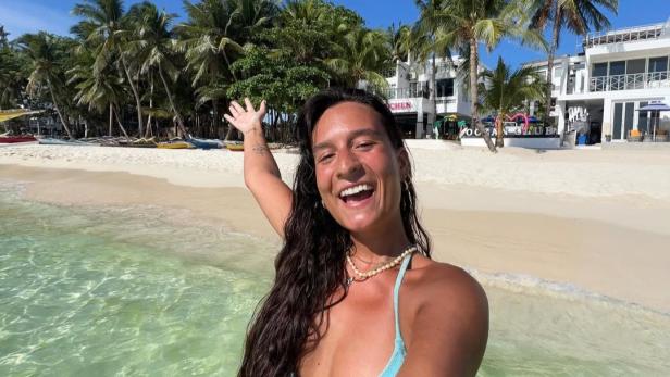 Vanessa Konopka: 28-jährige brünette Frau posiert lachend vor einem Strand