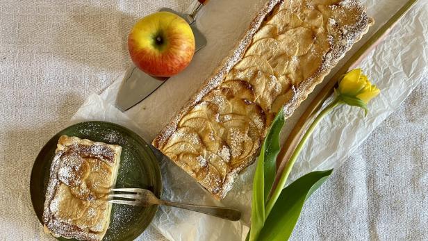 Ein Apfel-Rhabarber-Kuchen neben einer gelben Blume und einem Apfel.