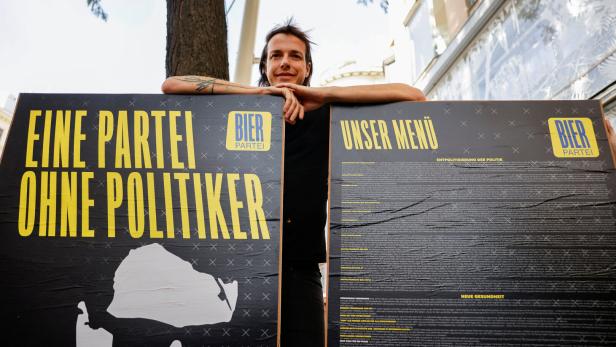 Bierpartei-Gründe Dominik Wlazny  vor Wahlplakaten für die Nationalratswahl, auf ihnen steht: Eine Partei ohne Politiker 