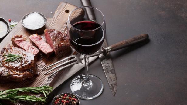 Ein Steak, tranchiert auf einem Holzbrett, mit einem Glas Rotwein und Gewürzen angerichtet.