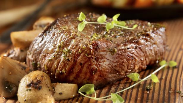 Ein saftiges Steak mit Pilzen auf einem Holzbrett angerichtet.