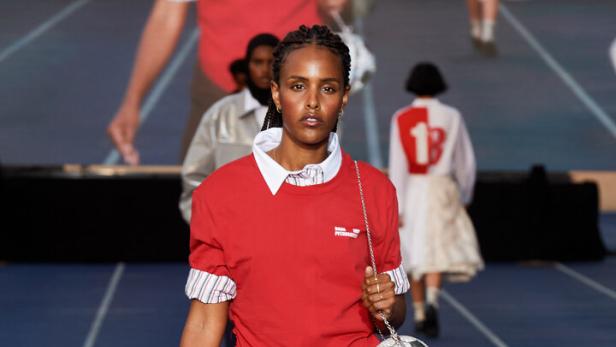 Eine Frau in Sportkleidung mit einer Handtasche in Form eines Fußballs auf einem Laufsteg.