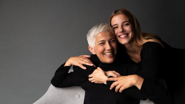 Eine junge Frau umarmt lachend eine ältere Frau mit kurzen, grauen Haaren.