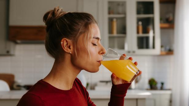Seitenansicht einer schönen jungen Frau, die frischen Saft in der Küche genießt.