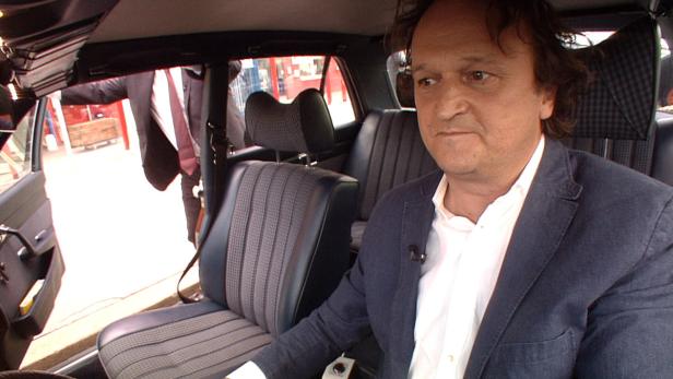 Ein Mann sitzt in einem Auto mit blau-grauen Sitzen.