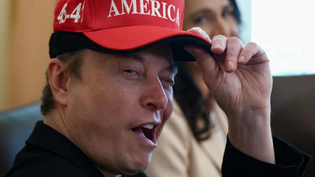 Elon Musk trägt eine bescheuerte Kappe und zwinkert teuflisch in die Kamera.