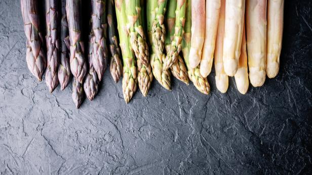 Verschiedene Sorten Spargel liegen auf einer dunklen Oberfläche.