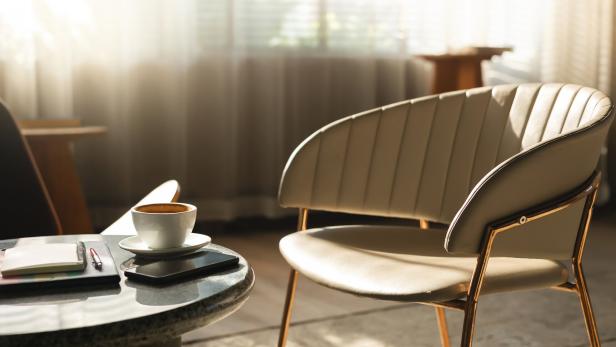 Eine Tasse Kaffee, ein Notizbuch und ein Smartphone auf einem Tisch neben einem Sessel.