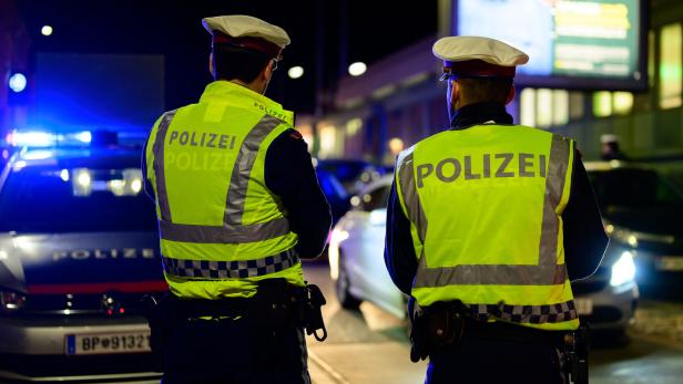 Polizisten stehen nachts vor ihren Polizeiautos.