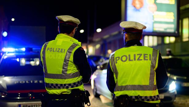 Polizisten stehen nachts vor ihren Polizeiautos.