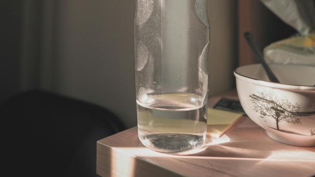 Wasserflasche auf Holztisch Wasserflasche mit nur mehr wenig Wasser steht an der Kante eines Holztisches