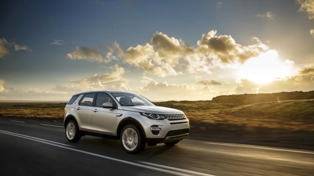 Ein silberner Land Rover Discovery fährt auf einer Straße bei Sonnenuntergang.