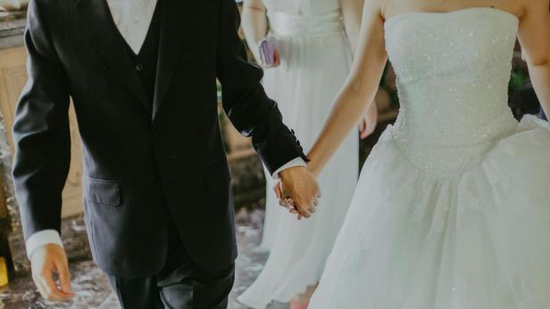 Frau im weißen Brautkleid Hand in Hand mit Mann im schwarzen Anzug