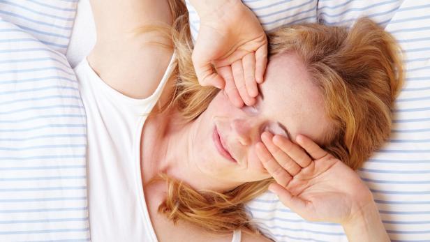 Frau reibt sich im Bett die Augen.