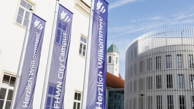 Flaggen mit der Aufschrift „Herzlich Willkommen!“ und „FHWN City Campus“ vor modernen Gebäuden.