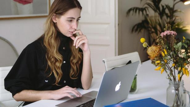 Eine Frau sitzt an einem Tisch und arbeitet an einem Laptop.