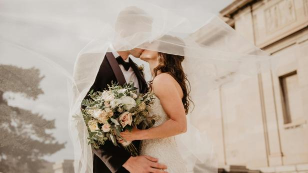 Hochzeitspaar küsst sich unter Brautschleier.