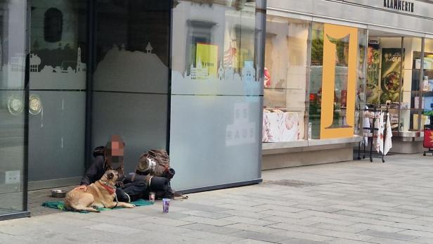 Mann sitzt mit Hund auf Gehsteig 