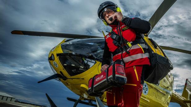 Ein Mann in roter und gelber Kleidung steht neben einem Hubschrauber.