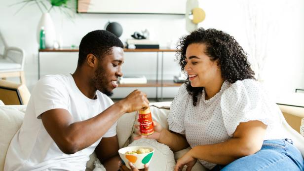 Pärchen sitzt auf Couch und isst Snacks