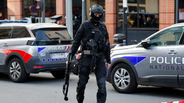 Ein Polizist in voller Montur steht vor Polizeiautos in Frankreich.