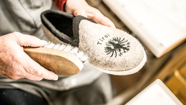 Eine Person bürstet einen grauen Filzpantoffel mit Tiroler Adler-Emblem.