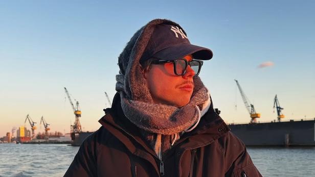 Alexander Runow posiert mit Kappe, Sonnenbrille und Schal am Hamburger Hafen
