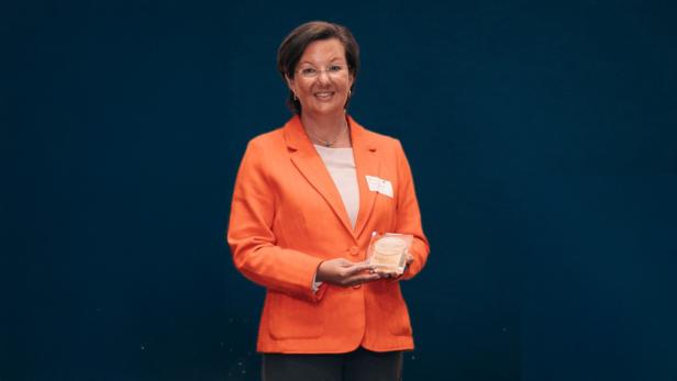Eine Frau in einem orangenen Blazer vor einer schwarzen Wand