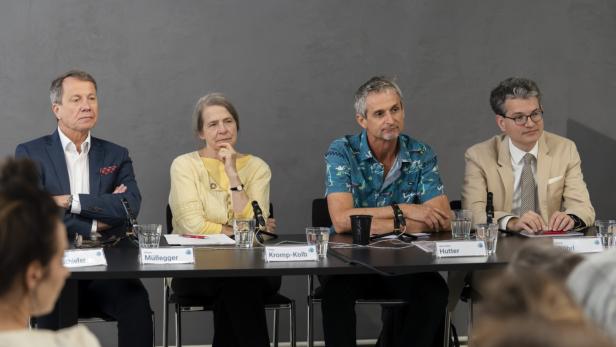 Im Bild sieht man vier Personen, drei Männer, eine Frau, die an einem Tisch sitzen.