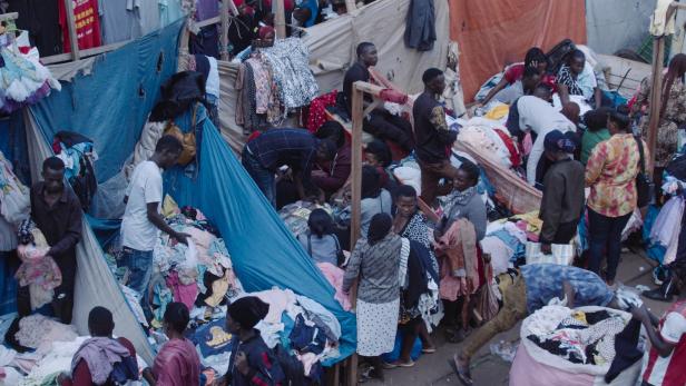 Verkäufer bieten auf einem Markt in Uganda Altkleider an. 