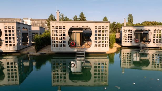 Moderne schwimmende Häuser mit dekorativen Fassaden spiegeln sich im Wasser.