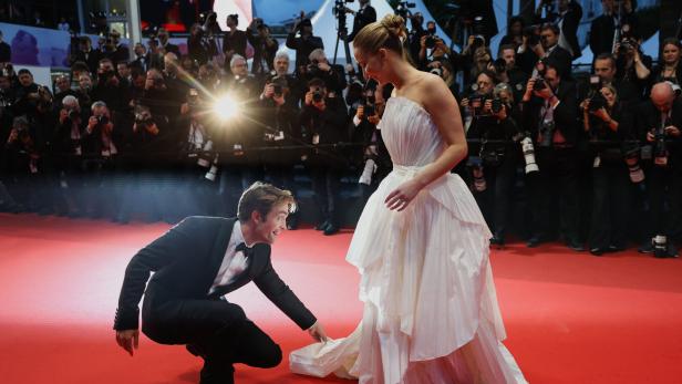 Robert Pattinson hilft einer Frau im weißen Kleid auf dem roten Teppich in Cannes.