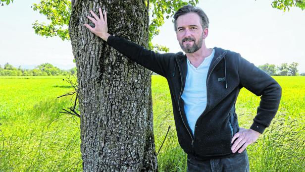 Reinhard Kaiser-Mühlecker lehnt an einem Baum auf einer Wiese.