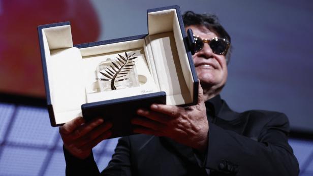 Ein Mann mit Sonnenbrille hält die Goldene Palme bei der Abschlusszeremonie der 78. Filmfestspiele von Cannes.