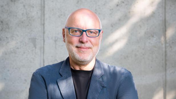 Porträt von Stefan Wallner mit verschränkten Armen vor einer Betonwand.