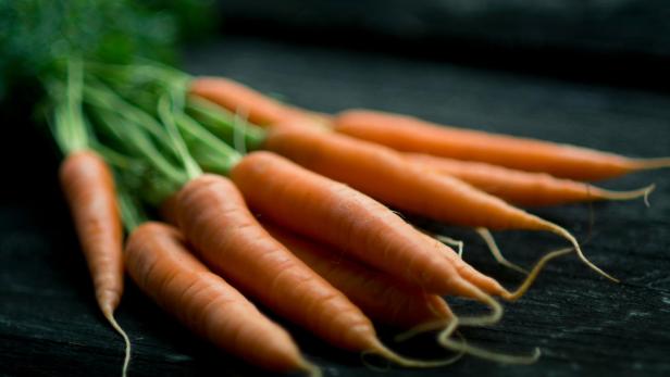 "Carrotmaxxing" soll Bräune ohne Sonnenbaden versprechen. Für eine Frau endete dieser Trend im Krankenhaus. Mehrere Karotten auf schwarzem Hintergrund